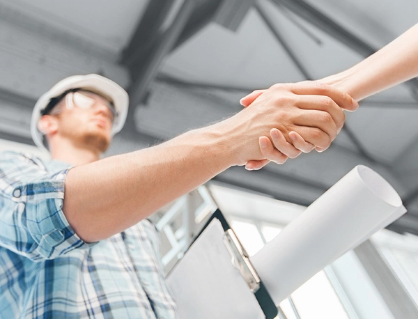 Worker wearing a hard hat and safety glasses shaking hands.