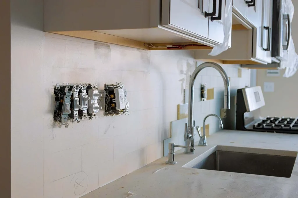 Unfinished kitchen with partially tiled backsplash and exposed light switches.